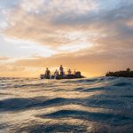 Sunset over tranquil waters with a silhouette of a boat, highlighting off-the-beaten-path travel experiences in Honduras.