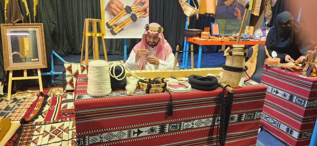 Local artisan demonstrating traditional weaving techniques in Riyadh, surrounded by crafts and textiles, showcasing Saudi Arabia's cultural heritage.