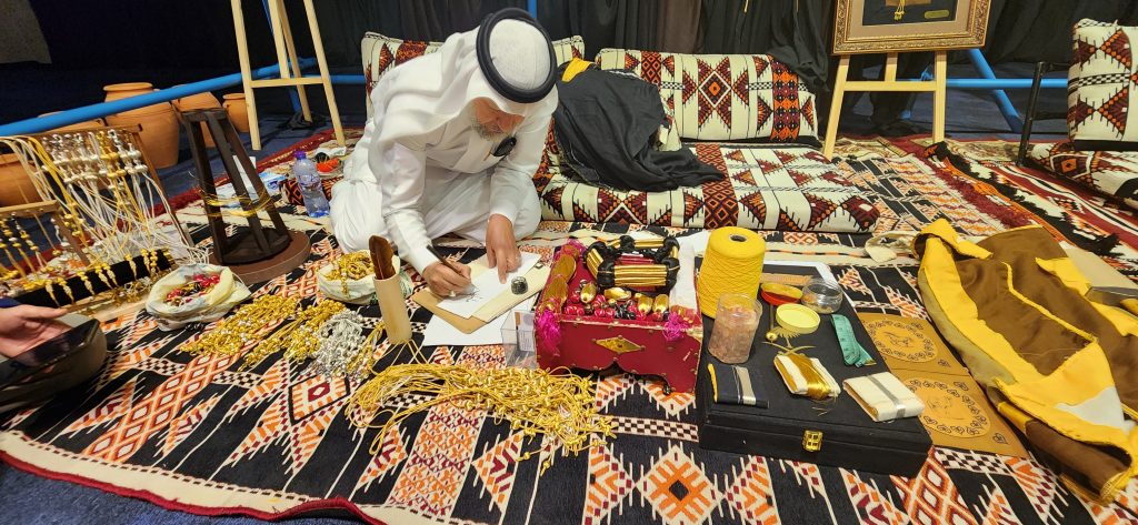 Craftsman creating intricate jewelry designs surrounded by traditional Saudi materials, showcasing cultural heritage and craftsmanship in a vibrant market setting.