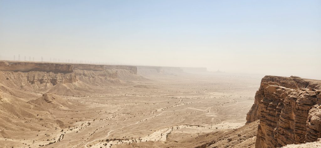 Vast desert landscape of AlUla, featuring sandstone cliffs under a clear sky, capturing the tranquility and natural beauty of Saudi Arabia's wilderness.