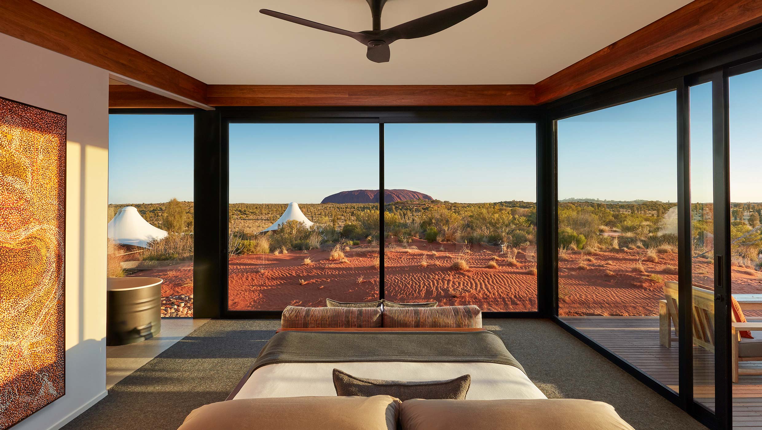 Luxury lodge interior with a view of Uluru, featuring a comfortable bed, modern decor, and a serene desert landscape outside.