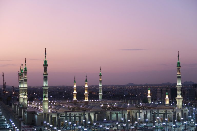 Mosque with illuminated minarets at dusk in Saudi Arabia, showcasing cultural and architectural beauty relevant to a travel journey.