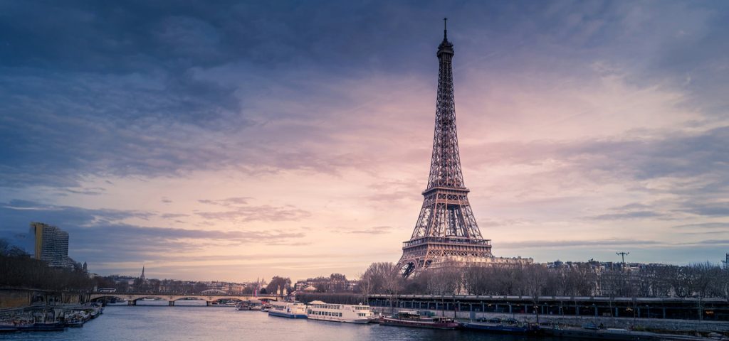 Eiffel Tower in Paris at sunset, overlooking the Seine River, with a serene sky and cityscape, representing unique travel experiences in France.