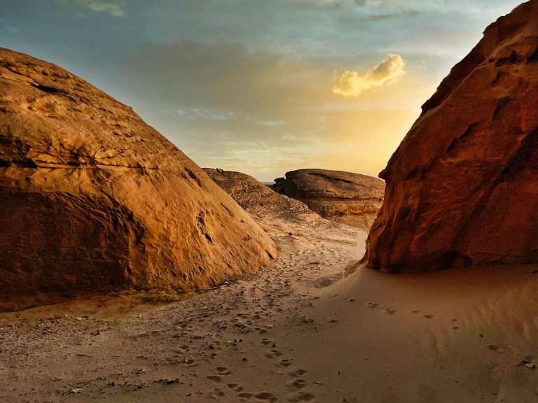 Desert landscape with towering rock formations and sandy path, reflecting the diverse natural beauty of Saudi Arabia, ideal for cultural exploration and adventure travel.