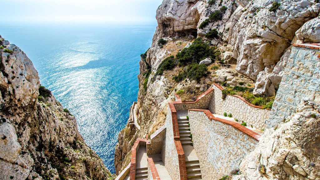 Stunning coastal staircase leading to the Mediterranean Sea, surrounded by rocky cliffs and vibrant blue water, highlighting unique travel experiences in off-the-beaten-path destinations.
